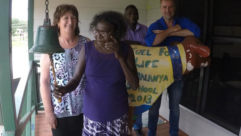 An Indigenous woman ringing a bell in foreground with three people behind her.