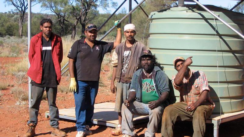 Five Indigenous men in front of a water tank