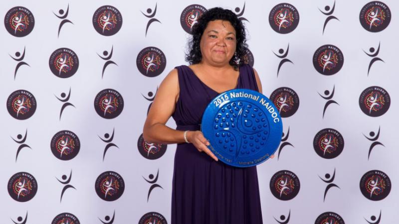 Indigenous woman Michelle Deshong holding blue plate shaped award.