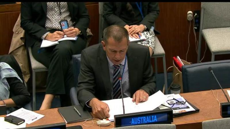 Mike Fordham reading from a text while seated at a bench in the United Nations general assembly room