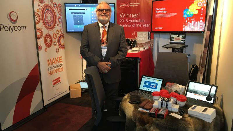 Indigenous man in suit standing amongst display of posters and technical equipment.