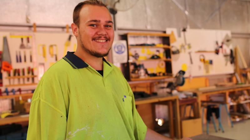 Man in safety vest stands in wood workshop