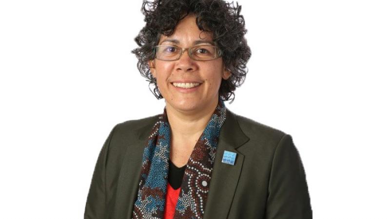 Aboriginal woman wearing glasses, a dark jacket and scarf covered with Indigenous designs.