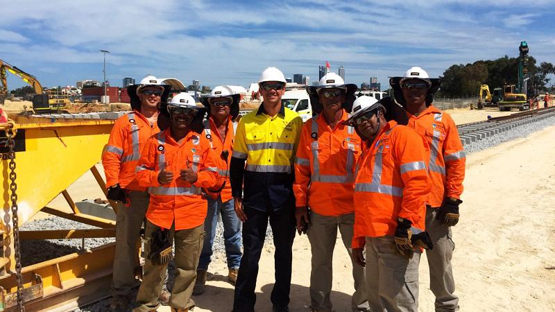 A group of seven men at a construction site, wearing high-vis vests and hard hats.