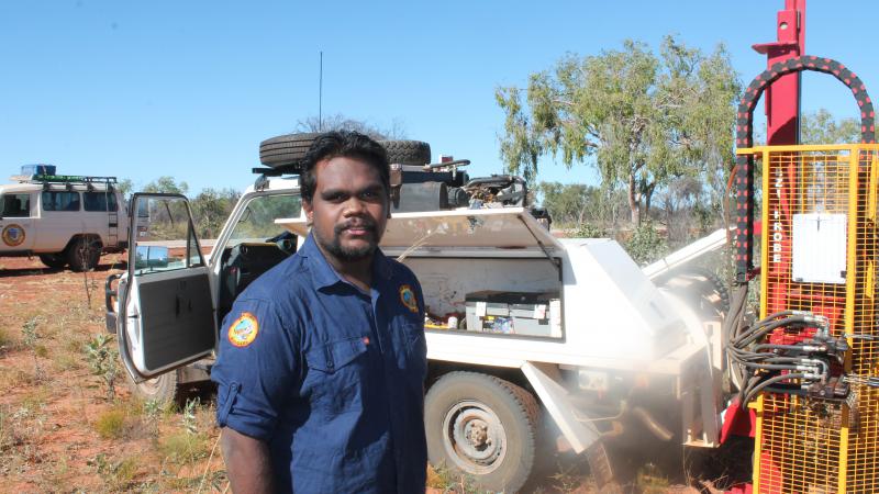 A young Aboriginal man, Wynston Shovellor-Sesar, stands in front of vehicle and other machinery.