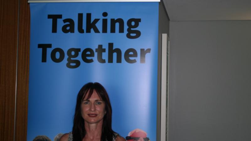 Woman standing in front of poster with displayed words, Talking Together