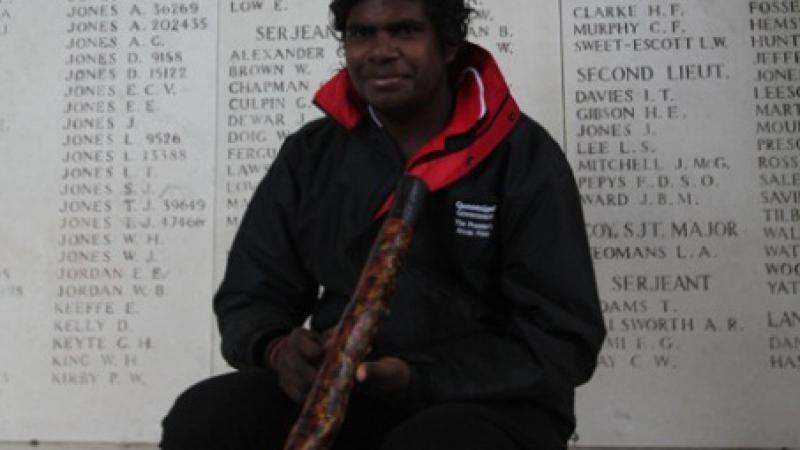 Elijah Douglas, holding his didgeridoo, sits in front of a wall of remembrance.