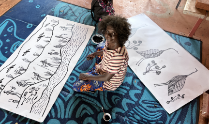 An artists sits on floor between two artwork prints