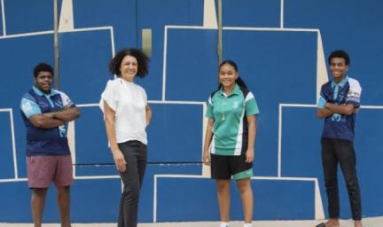 3 youth and an adult woman stand on a carpeted floor. Behind them is a blue wall with white designs.