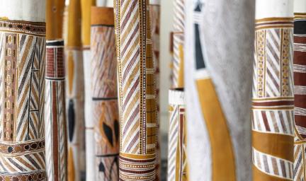 Many wooden poles painted in traditional styles stand upright in a group.