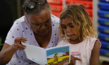 A mature woman and a young girl hold a picture book between them and read.